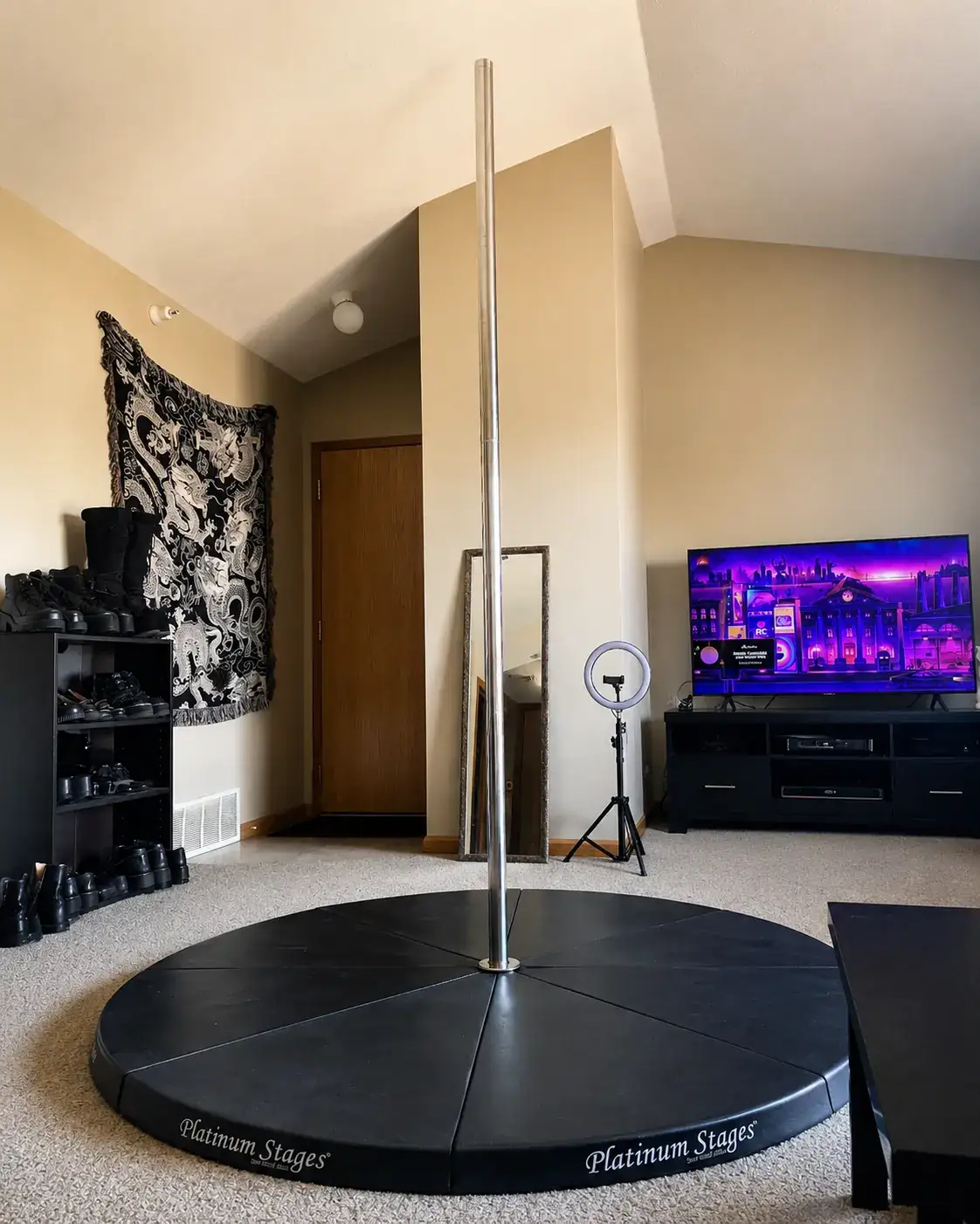 Self-standing chrome dance pole set up on a black stage in a cozy living room